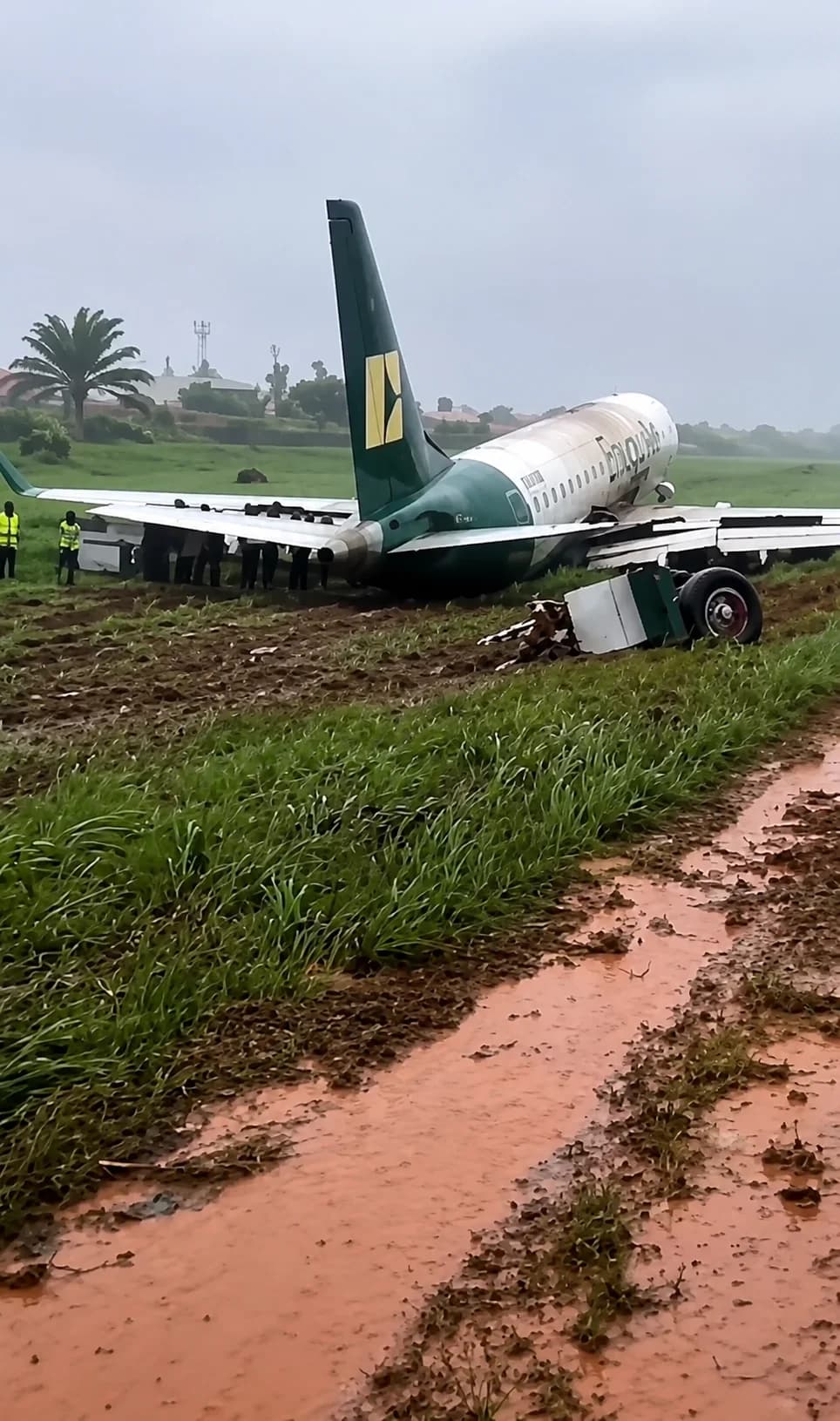 An Enugu Air Embraer E170 resting off the runway at Benin Airport after a runway excursion, surrounded by emergency responders.