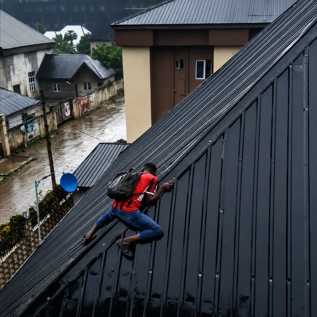 Solar panel installer climbing down from a rooftop during heavy rain in Nigeria.
